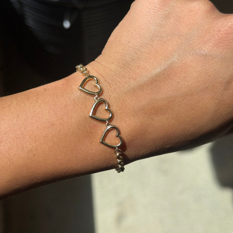 A vintage yellow gold triple heart bracelet shown worn on a person's wrist
