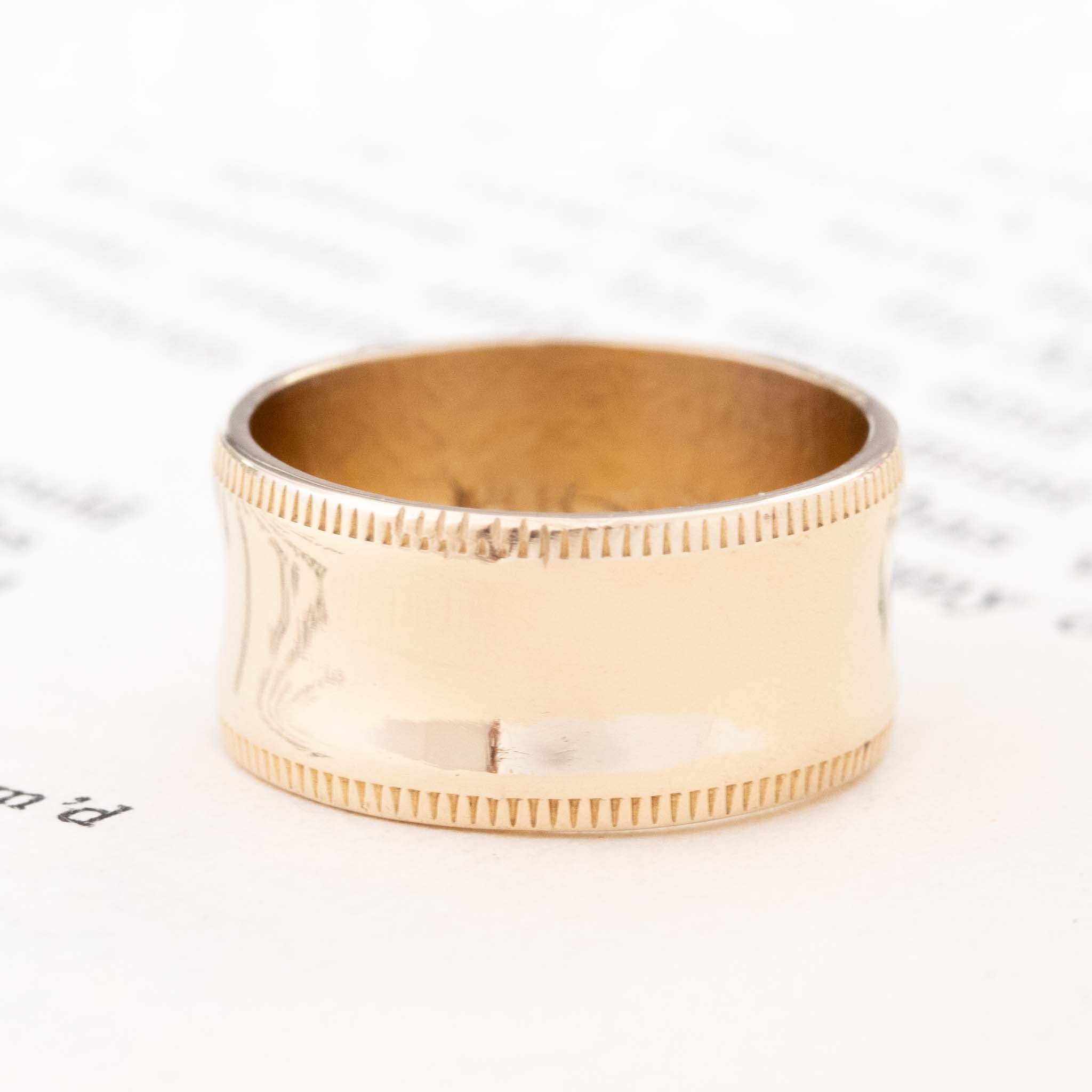 14kt yellow gold wide wedding band with a concave center and milled edges.